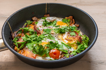 Fresh rustic breakfast - fried egg with bacon, onion and cherry tomatoes in a pan
