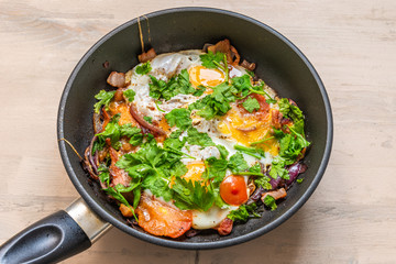 Fresh rustic breakfast - fried egg with bacon, onion and cherry tomatoes in a pan