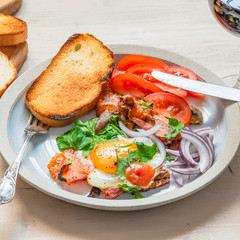 Fresh rustic breakfast - fried egg with bacon, onion and tomatoes on a plate  and toast on a light wooden background, close-up