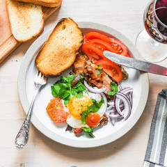 Fresh rustic breakfast - fried egg with bacon, onion and tomatoes on a plate  and toast on a light wooden background, close-up