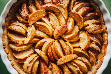 Baked apple pie in ceramic bowl on table with green tablecloth