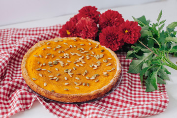 Homemade pumpkin pie on white plate with napkin and red flowers
