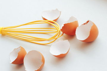 Brown eggshell and whisk on wooden background
