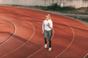 Caucasian female runner in sportswear running on the stadium with earphones in ears.