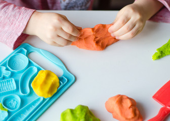 Obraz na płótnie Canvas Child's hands with colorful clay. Child playing and creating vagetables from play dough. Girl molding modeling clay. Homemade clay..
