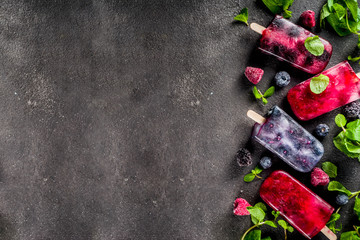 Fototapeta na wymiar Simple and healthy summer dessert. Homemade berry ice cream popsicles with mint. Mojito lollypops, frosen diet infused water with blackberry, blueberry and raspberry. Dark concrete background copy spa