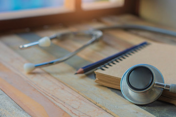 Notepad with stethoscope and pencil on wood board background.using wallpaper for education