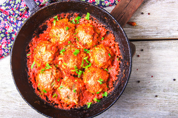 Meatballs in tomato sauce garlic and parsley in an iron frying pan on a white wooden background. Top view. Copy space
