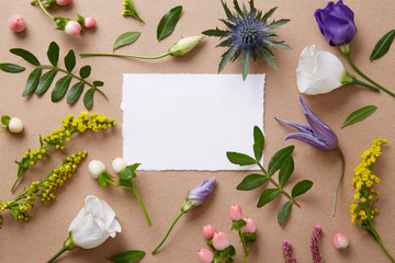 Blank paper decorated with various flowers and greenery. Greeting card on a neutral background. Top view. Copy space