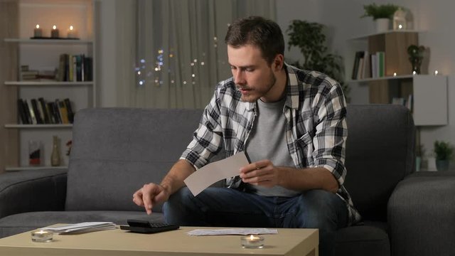 Sad man accounting checking receipts sitting on a couch in the night at home