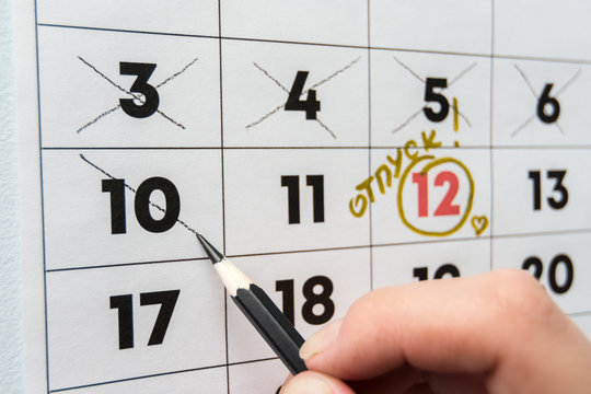 A hand crosses out the penultimate day before the holiday with a pencil in the calendar