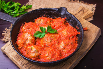 Meatballs in tomato sauce garlic and parsley in an iron frying pan on a dark brown wooden background. Top view. Copy space