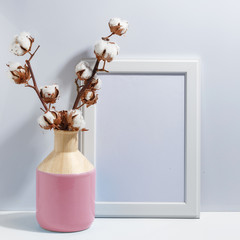 Mock up white frame and dry cotton twigs in pink on book shelf or desk. Minimalistic concept.