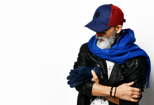 Old brutal senior rich man in leather jacket blue and red baseball cap and long blue scarf stands with gloves in arms stylish fashionable men 