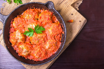 Meatballs in tomato sauce garlic and parsley in an iron frying pan on a dark brown wooden background. Top view. Copy space