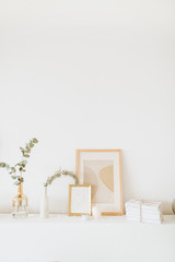 Styled interior design composition. Photo frame, eucalyptus branch, vase on white table. Trendy Scandinavian living room.