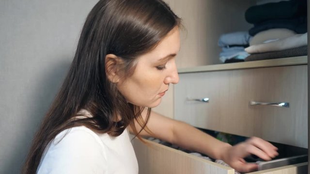 girl is looking for something among her things in a drawer in the closet