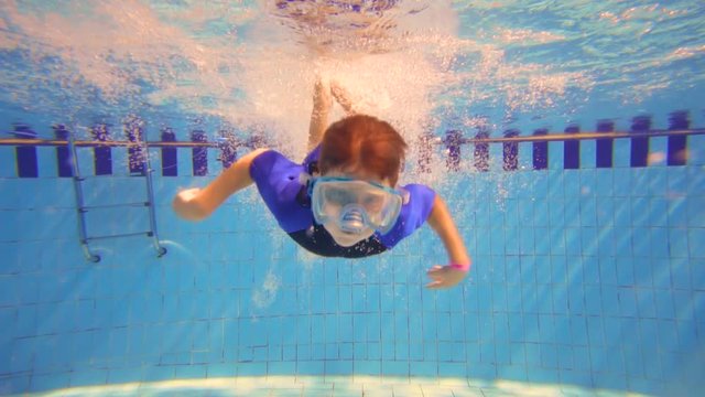 Boy in mask dive in swimming pool, underwater slow motion