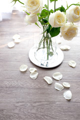 Romantic white rose in a glass vase on vintage silver plate and rose petals on wooden floor with white curtain background