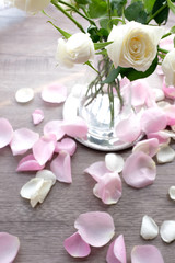 Obraz na płótnie Canvas Romantic white rose in a glass vase on vintage silver plate and white and pink rose petals on wooden floor with white curtain background