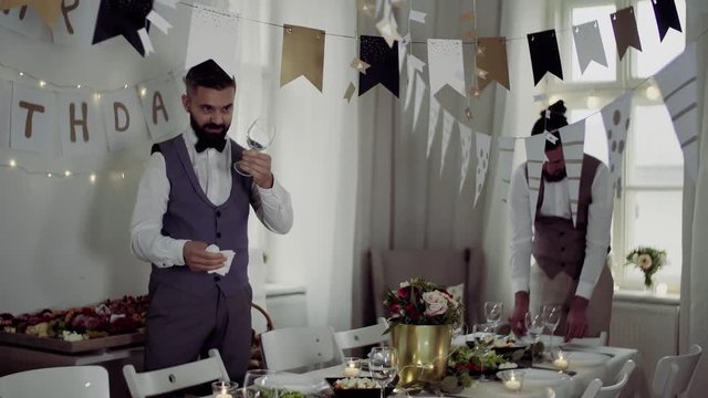 Two men with bows and vests setting a table for an indoor party.