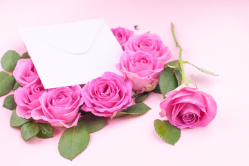 A bouquet of pink roses with petals on a pink background and a letter for text. Surprise in the concept of lovers day and mother's day. Flat lay. Copy space.