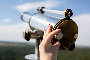 Female hand adjusts sharpness on a touristic telescope against forest panorama