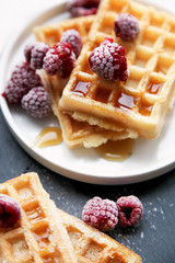 Home made waffles served with raspberries on stone and black background. Top view.