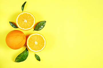 Close up image of juicy organic whole and halved oranges with green leaves & visible core texture, isolated yellow background, copy space. Macro shot of bright citrus fruit slices. Top view, flat lay.