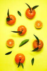 Close up image of juicy organic whole & halved tangerines with green leaves, visible core texture, isolated yellow background, copy space. Macro shot of bright citrus fruit slices. Top view, flat lay.