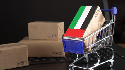 Paper box with a flag of United Arab Emirates in a shopping cart on a laptop keyboard. International E-commerce