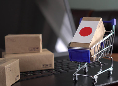 Parcel Boxes With A Flag Of Japan In A Shopping Cart On A Laptop Keyboard. Online Shopping