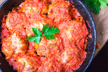 Meatballs in tomato sauce garlic and parsley in an iron frying pan on a dark brown wooden background. Top view. Copy space