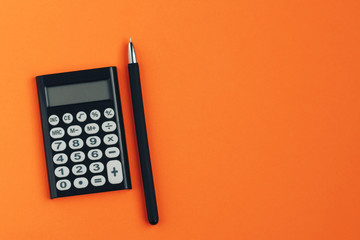 Calculator and pen on an orange background