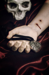 Pale white arm of a woman with a vampire bite, hand holding a heart-shaped pendant