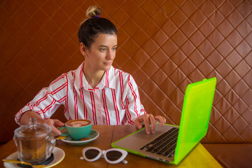 Young woman sitting in a coffee shop, having a coffee and working on her laptop.
