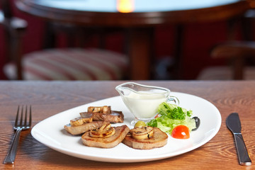 Mushrooms lie on fried beef tongue, olives and lettuce, cherry tomatoes and sour cream