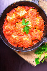 Meatballs in tomato sauce garlic and parsley in an iron frying pan on a dark brown wooden background. Top view. Copy space
