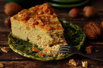 A piece of cheesecake with nuts on a green plate on wooden boards