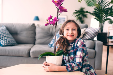 happy kid girl with orchid flower in pot. Modern living room with house plants