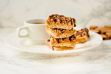 Paleo chocolate energy bars with rolled oats, nuts, dates caramel, chia seeds and coconut flakes. Horizontal.A cup of coffee.Tone.