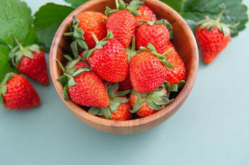 A bowl of beautiful and delicious strawberries isolated on a blue-green background, closeup, topview, copyspace.