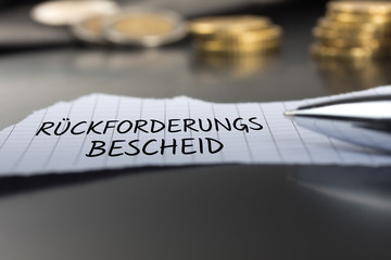 Rückforderungsbescheid auf einem Zettel mit Stift vor Geldmünzen