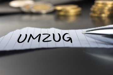 Umzug auf einem Zettel mit Stift vor Geldmünzen