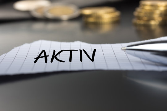 Aktiv auf einem Zettel mit Stift vor Geldm&uuml;nzen
