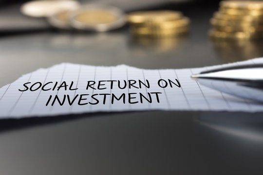 Social Return On Investment auf einem Zettel mit Stift vor Geldmünzen