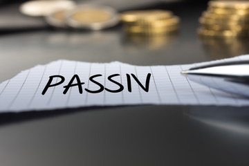 Passiv auf einem Zettel mit Stift vor Geldmünzen