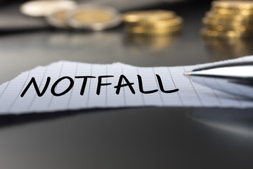 Notfall auf einem Zettel mit Stift vor Geldmünzen