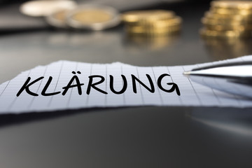 Klärung auf einem Zettel mit Stift vor Geldmünzen