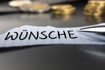 Wünsche auf einem Zettel mit Stift vor Geldmünzen
